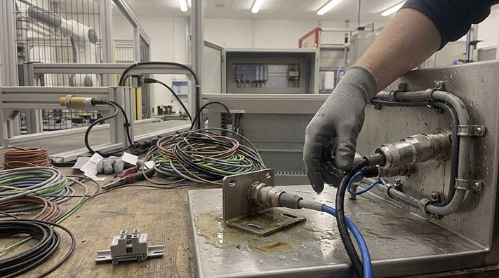 A stainless steel machine in a food processing plant being cleaned with a high-pressure spray.